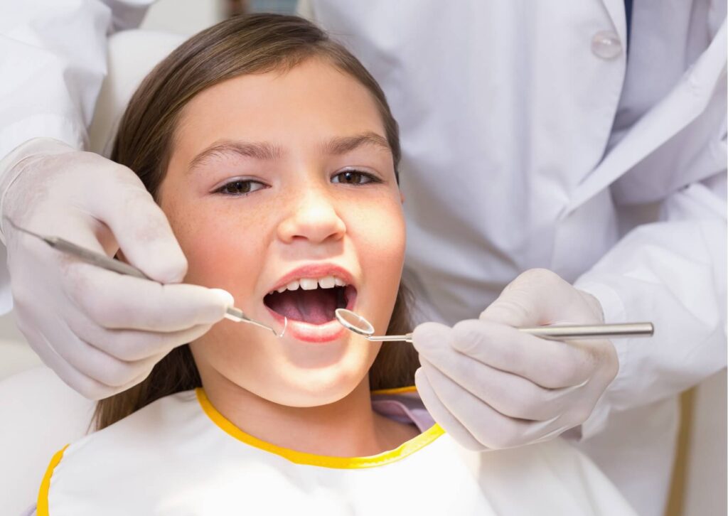 Pediatric dentist examining a child's teeth during a visit to monitor tooth development and determine if a kids dental spacer is appropriate.