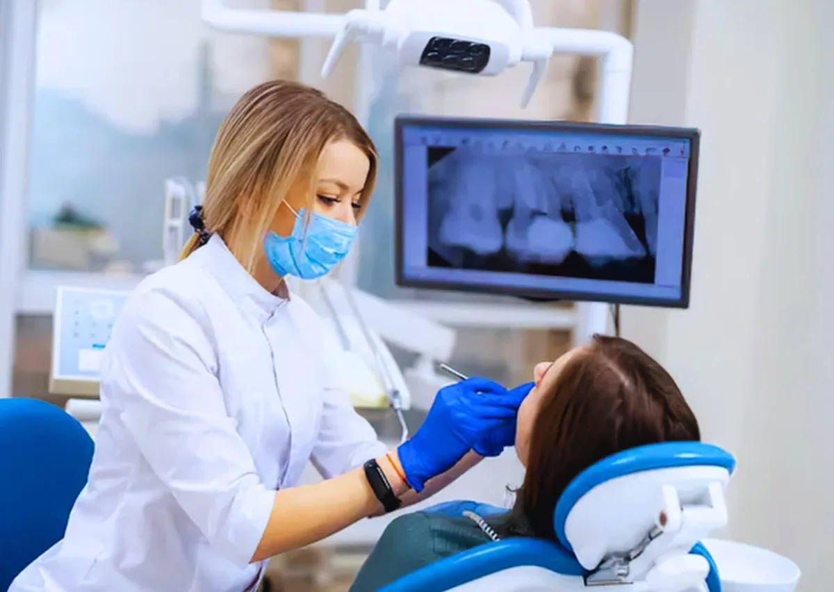 Dentist examining a patient's teeth with dental X-rays displayed on a monitor to assess eligibility for affordable dental implants.