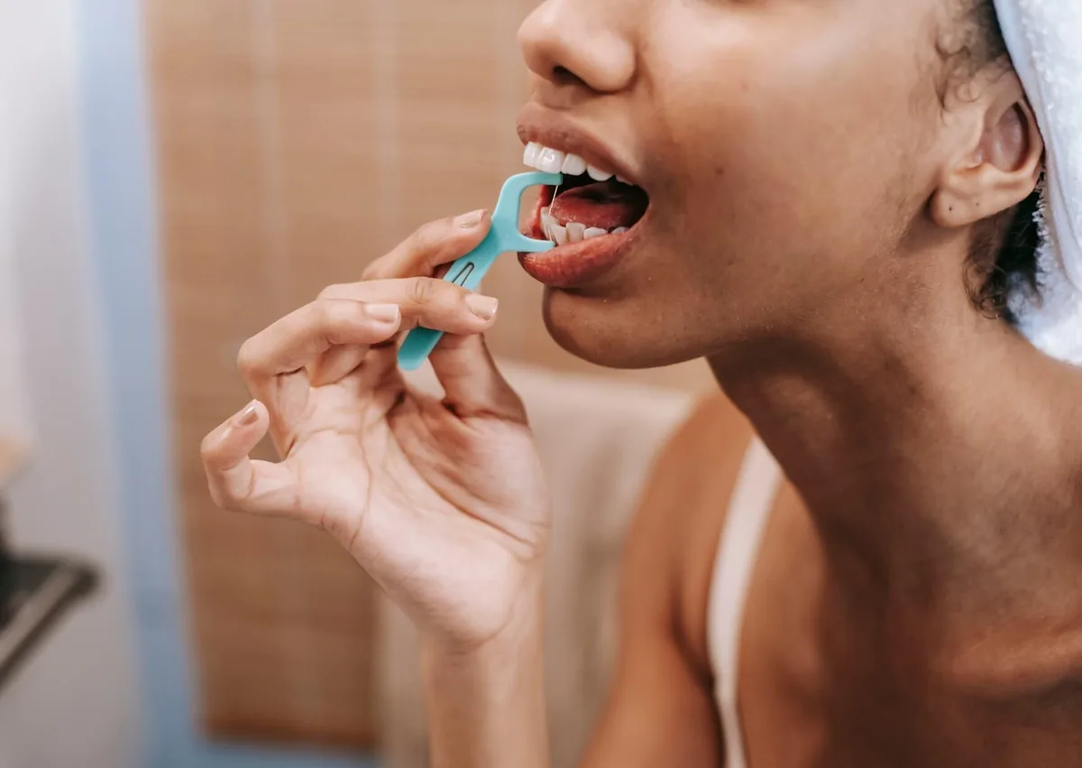 Woman flossing between her teeth to remove plaque and food particles, helping prevent cavities from forming over time.